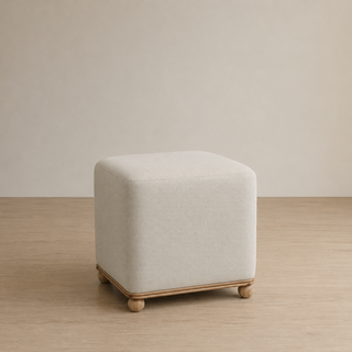 Beige cube-shaped ottoman on a wooden floor with a plain wall background
