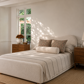 Neatly made bed with decorative pillows in a bright bedroom with a window.